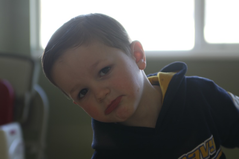 A young child facing away from a window, face looks dark