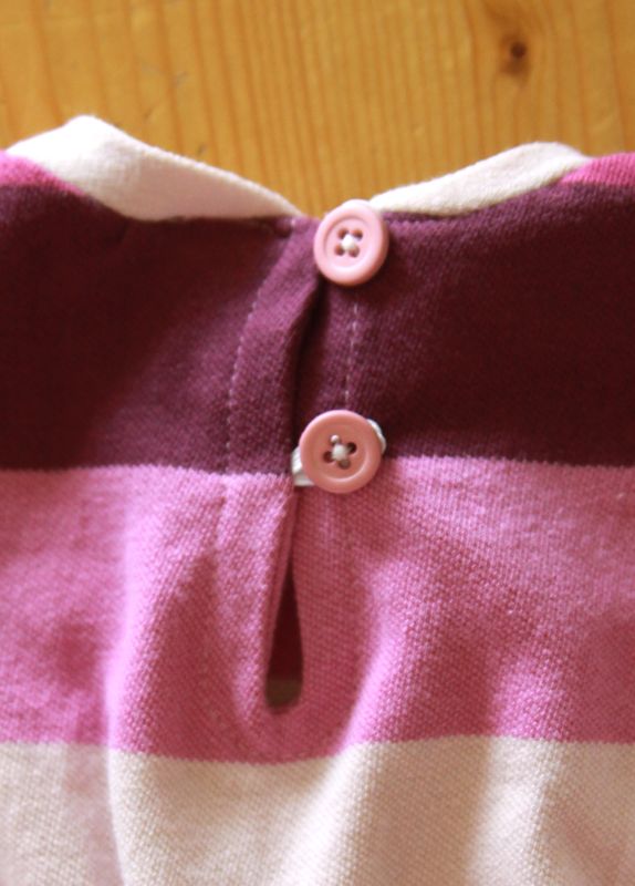 A close up of a purple baby dress with button closure on the back