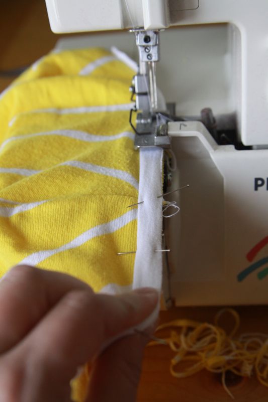 white fabric strip pinned over yellow fabric on sewing machine, white fabric stretch so yellow fabric lays flat