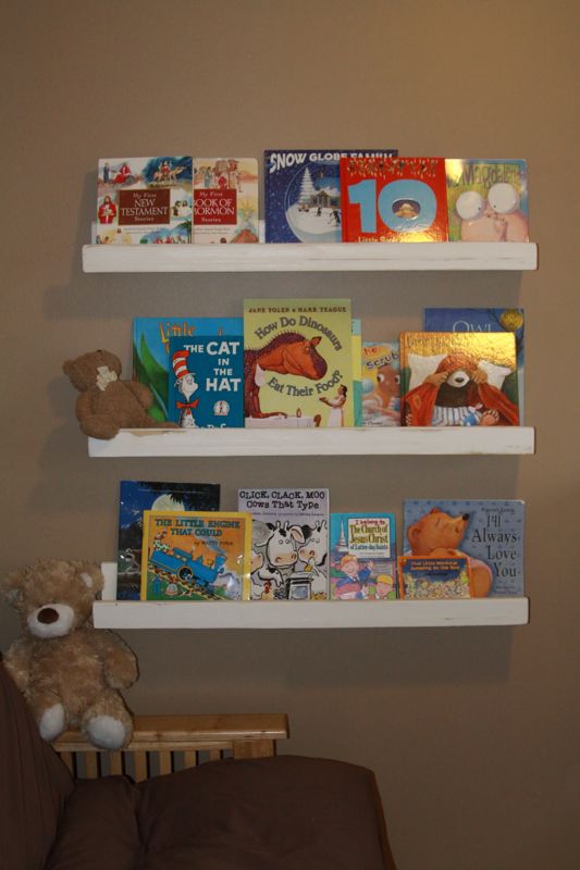 Three white wood shelves on a wall with picture books on them