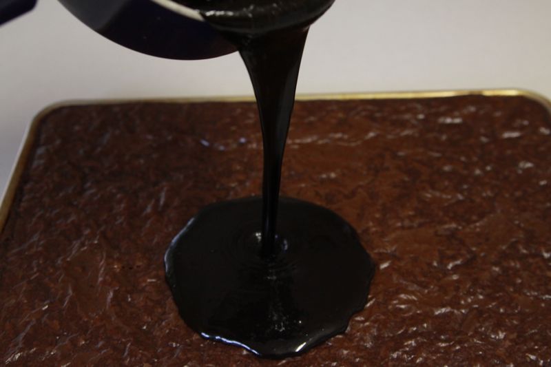 dark chocolate frosting being poured onto brownies