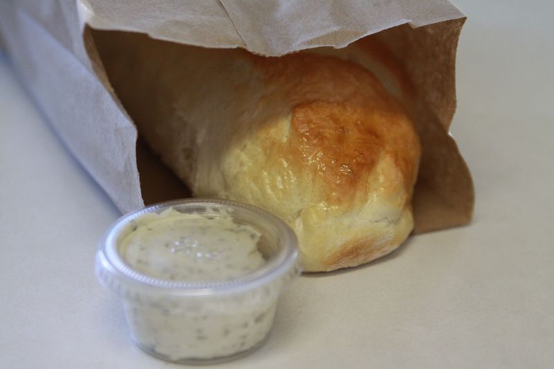 A loaf of french bread in a lunch sack with plastic container of garlic spread