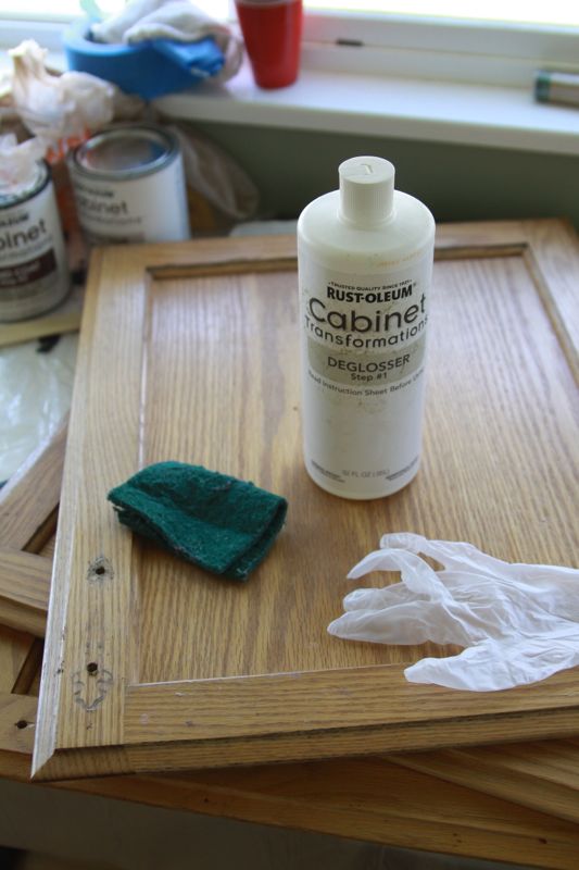 A close up of a bottle of deglosser on a cabinet door with scrubbing pad and glove