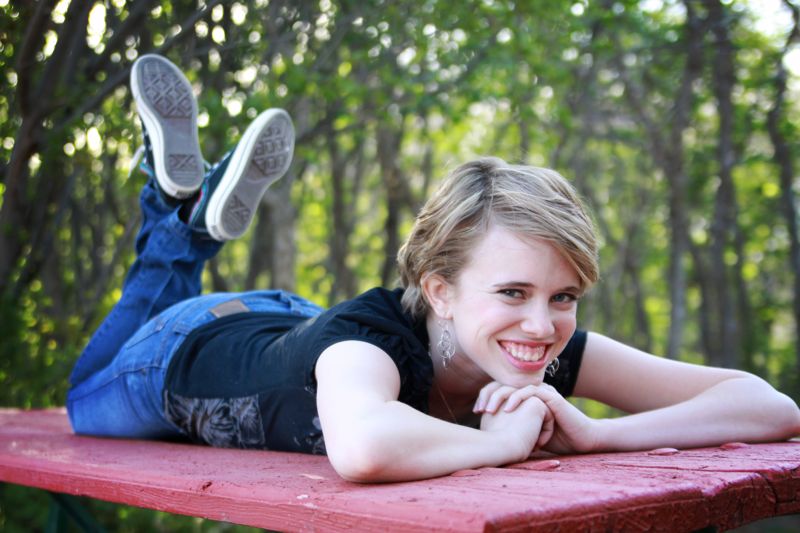 A girl lying on a picnic table with her chin on her hands and her feet kicked up behind her