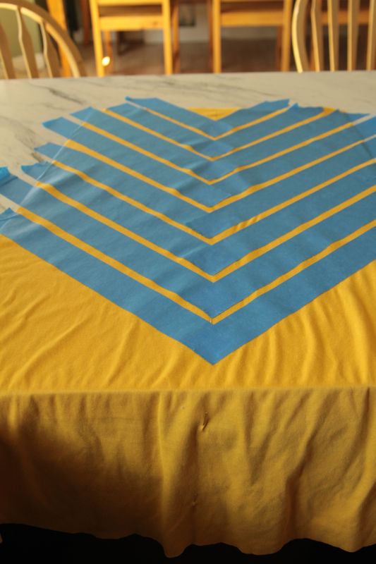 A piece of yellow fabric with painters tape on it making chevron print