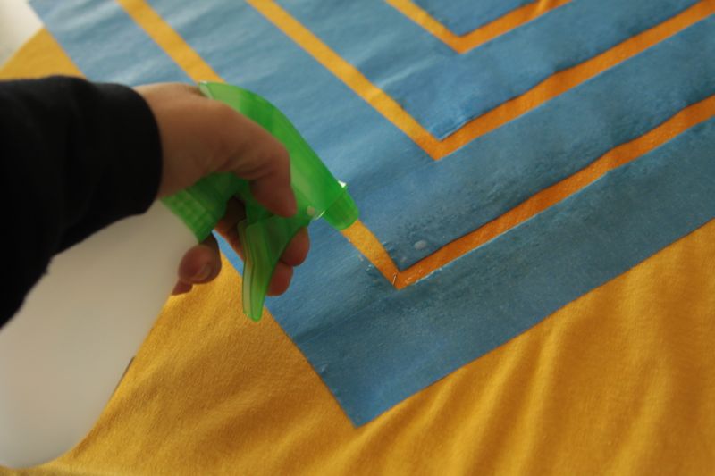 Hand holding spray bottle, spraying at fabric in between the painters tape