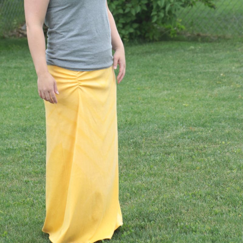 A person standing on grass wearing a yellow maxi skirt with ruching at the hip