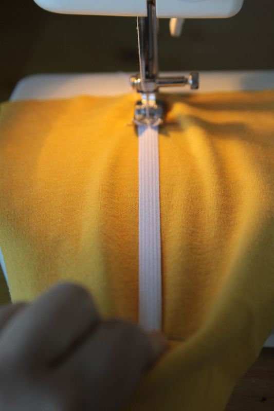 Yellow fabric and elastic on sewing machine with elastic stretched so fabric is flat