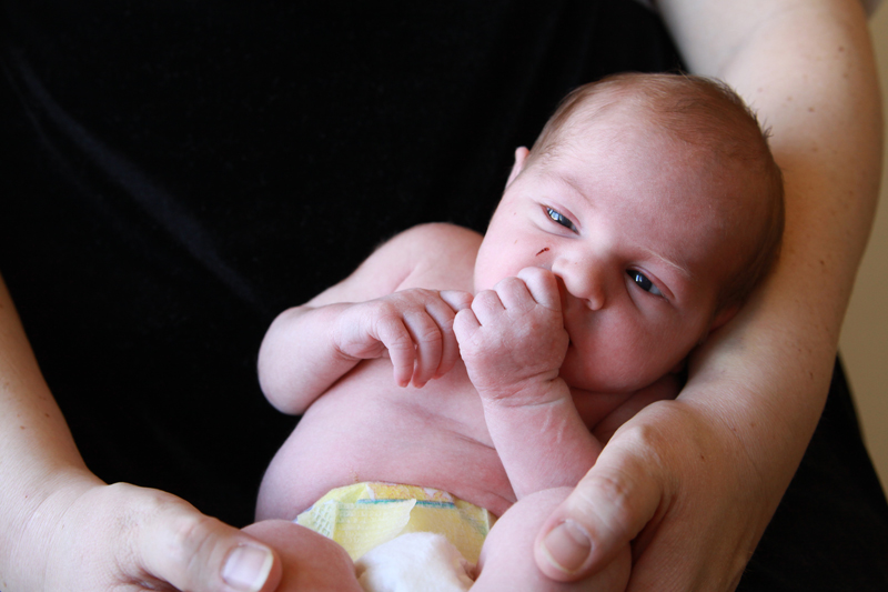 Closeup photo of a baby in a diaper, baby has hand in his mouth