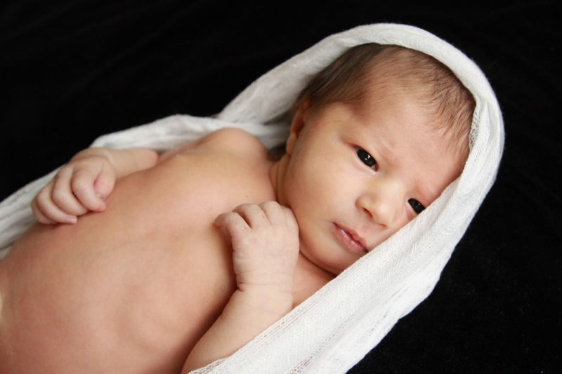 A baby lying on a bed wrapped in white fabric