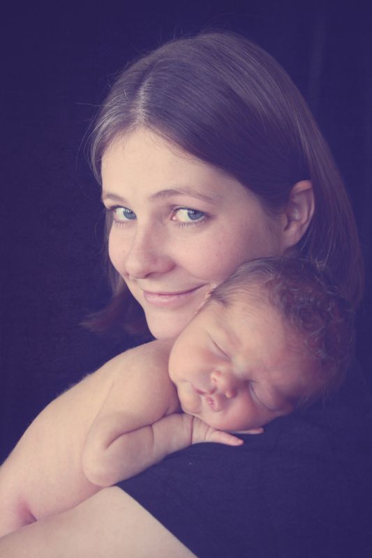 A mom holding a baby up on her shoulder, looking at the camera