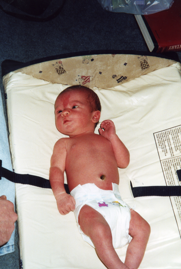 A old, poorly lit photo of a newborn baby in a bassinet