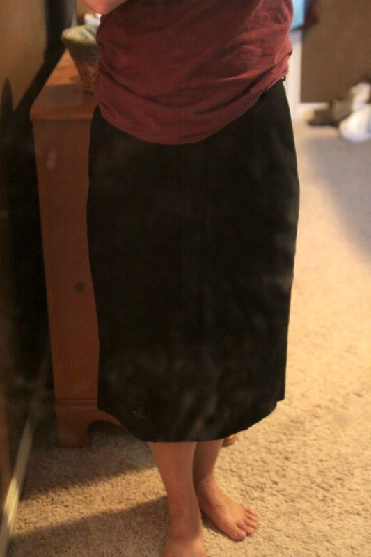 A person standing in a long black skirt with hem marked beneath knee