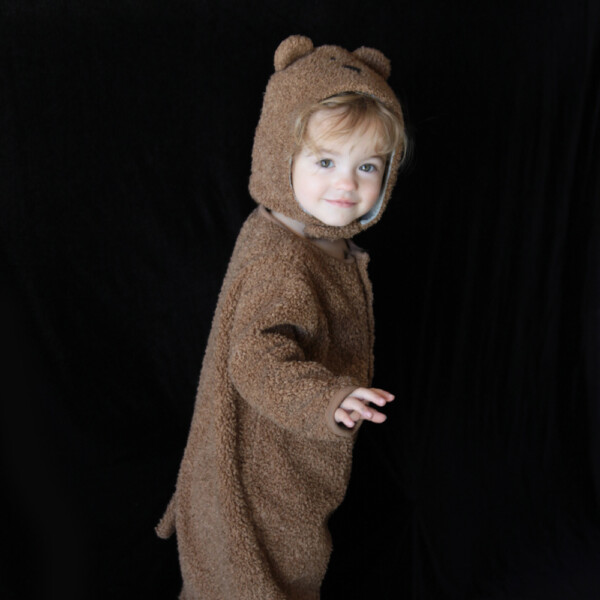 A little girl in a teddy bear costume with a plain black background
