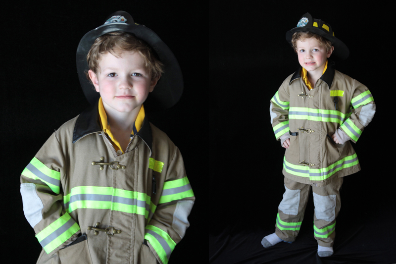 A young boy in a firefighter costume standing in front of a black background