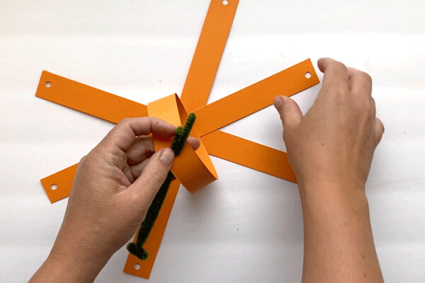 Pulling up the first two strips and threading the pipe cleaner through the holes