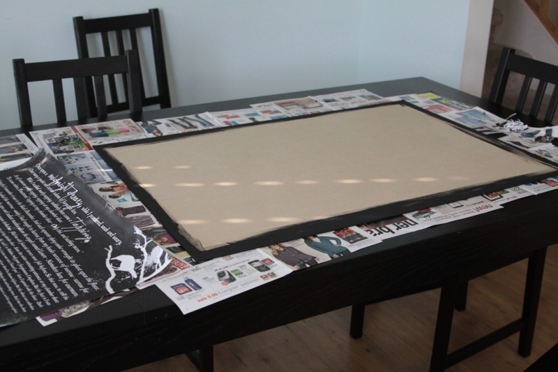 A large piece of MDF painted black around the edges on table covered in newspapers