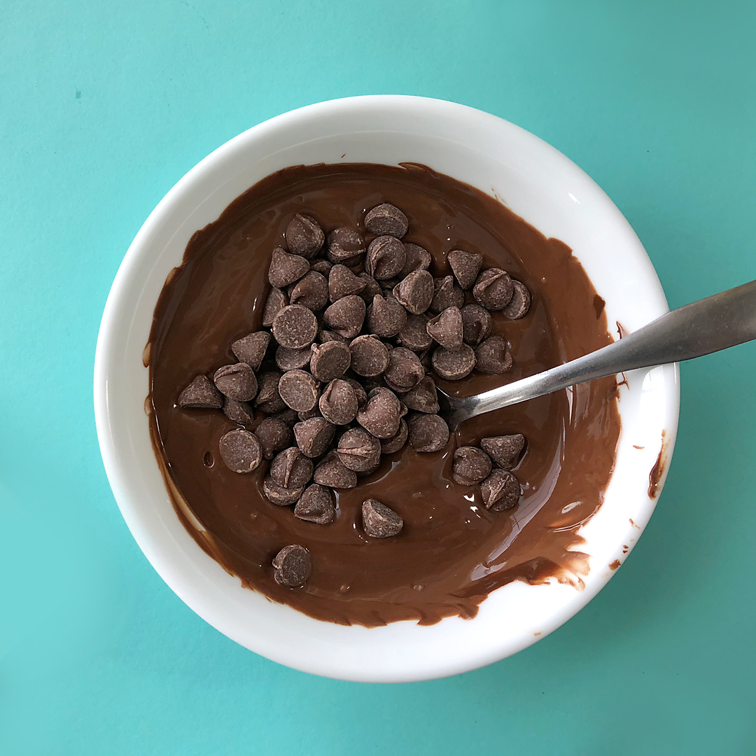 A bowl of melted chocolate chips with a handful of unmelted chocolate chips on top