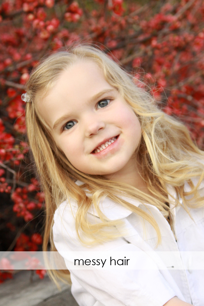 A little girl smiling at the camera with messy hair across her neck