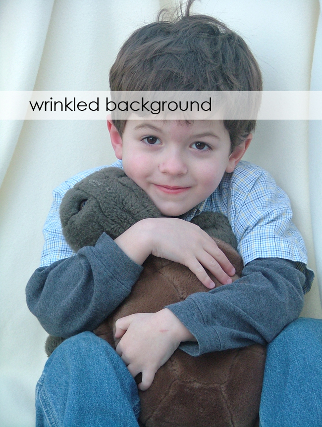 A little boy holding a teddy bear with a wrinkled blanket background