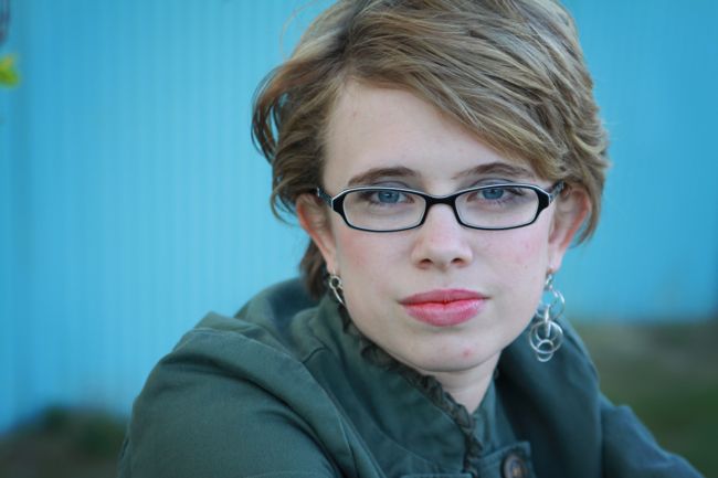 A person in glasses looking at the camera, with very blurry blue background bokeh