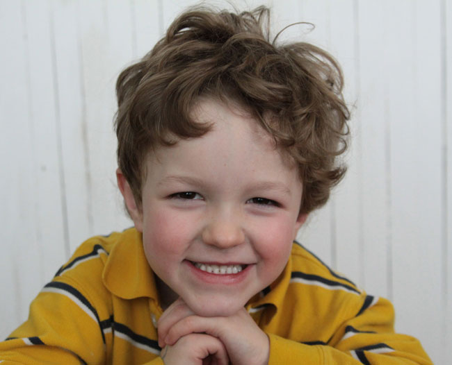 LIttle boy smiling in front of a white wood background