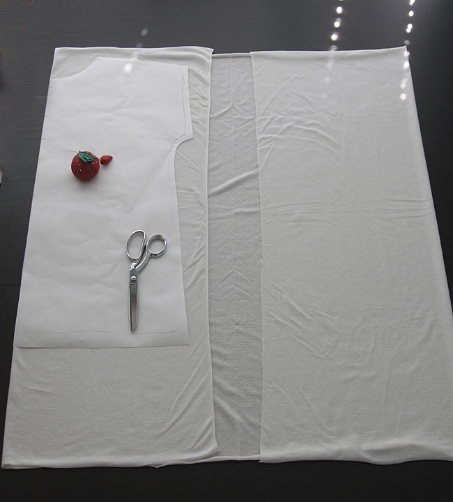 Shirt pattern laid over white knit fabric, with pin cushion and sewing scissors
