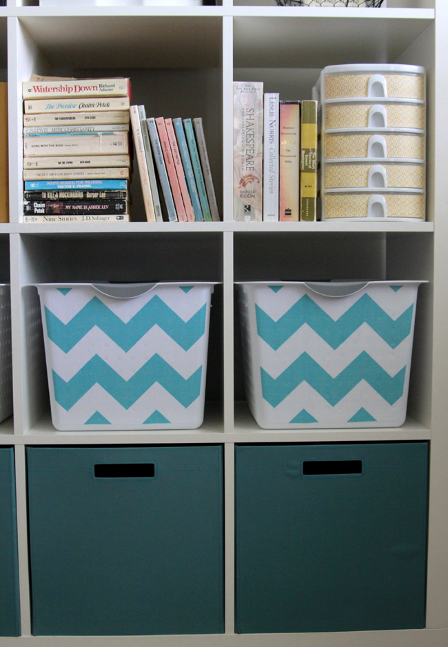 A close up of a cube storage unit with white bins that have been covered with turquoise chevron fabric