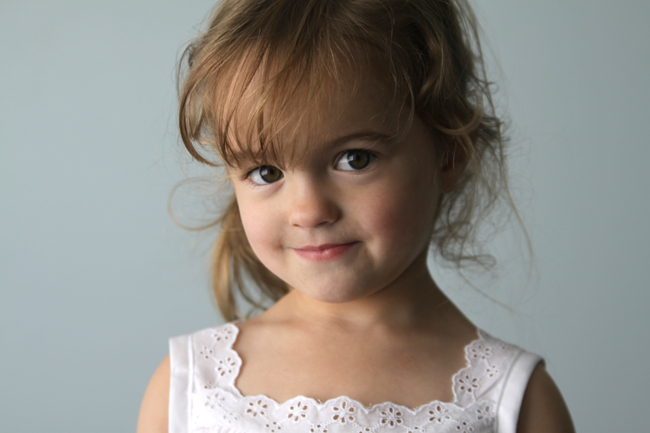 A little girl posing for a picture wearing a lace trimmed blouse
