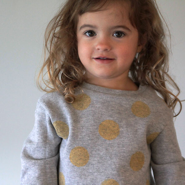 A little girl wearing a grey sweatshirt with gold polka dots