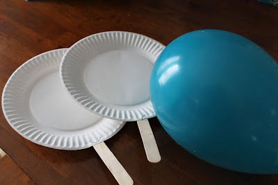 A blown up balloon and two paddles made from paper plates and popsicle sticks