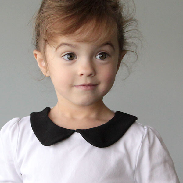 A little girl in a white shirt with a black peter pan collar