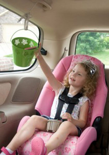A little girl sitting in a car seat reaching for a bucket that hangs in front of her