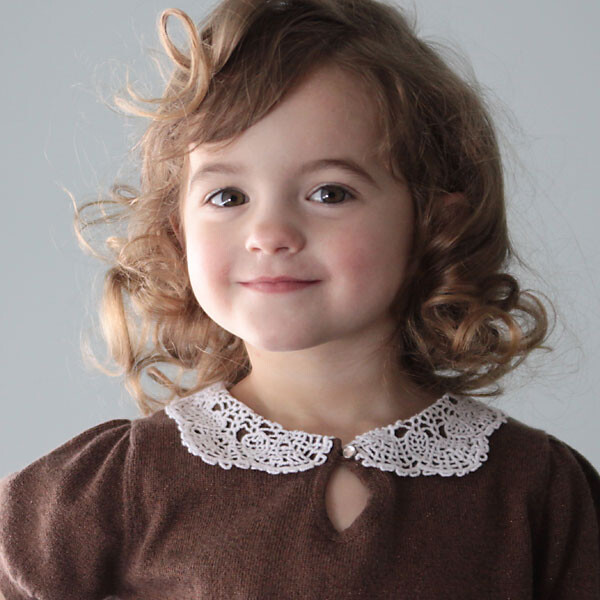 A little girl wearing a brown shirt with a doily collar