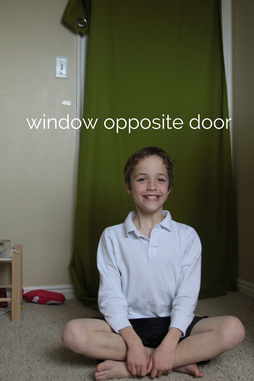 Little boy sitting in a bedroom with green curtain panel hanging on a door behind him