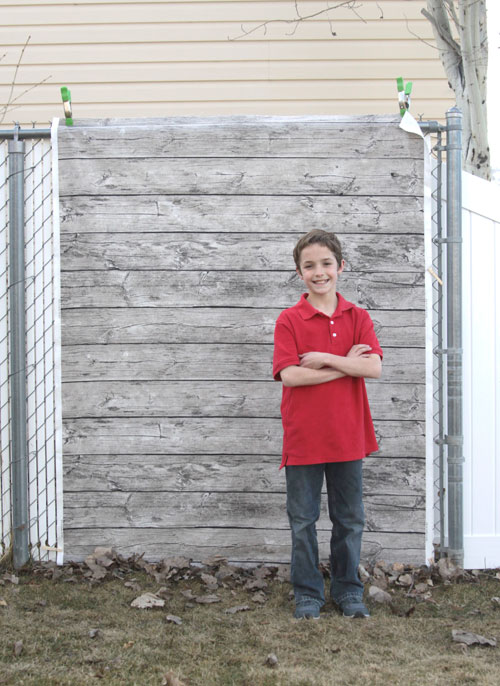 A little boy standing in front of fabric that looks like a wood wall
