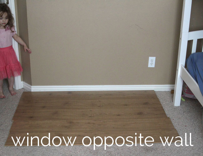 laminate flooring placed over carpet up against a bedroom wall