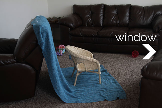 A wicker chair set up across from a window with a blue blanket draped behind it
