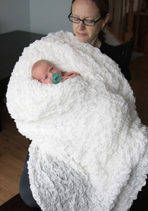 Mom covered with textured white blanket, holding baby wrapped in blanket