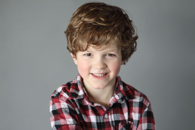 A young boy looking at the camera with flat gray background