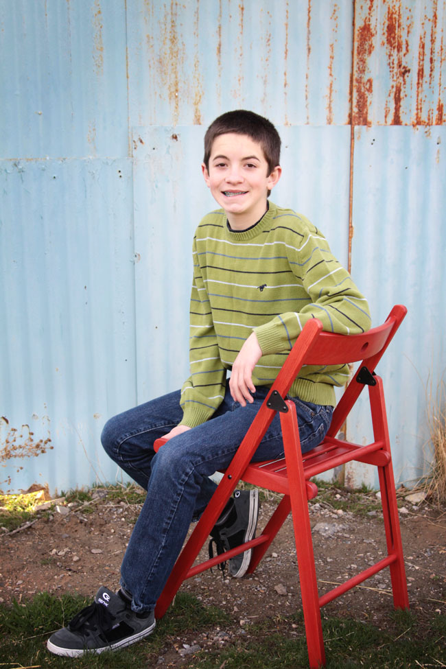 A boy sitting on a red chair in front of a blue corrugated wall