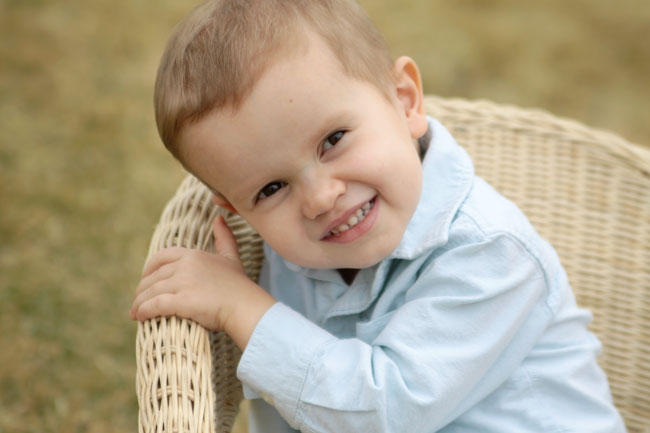 A little boy sitting in a wicker chair on the grass