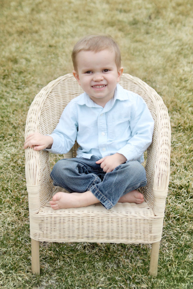 A small child sitting in a wicker chair on the grass