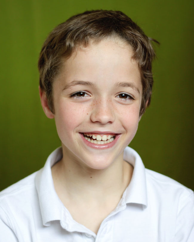 A young boy who is smiling at the camera in front of a green background