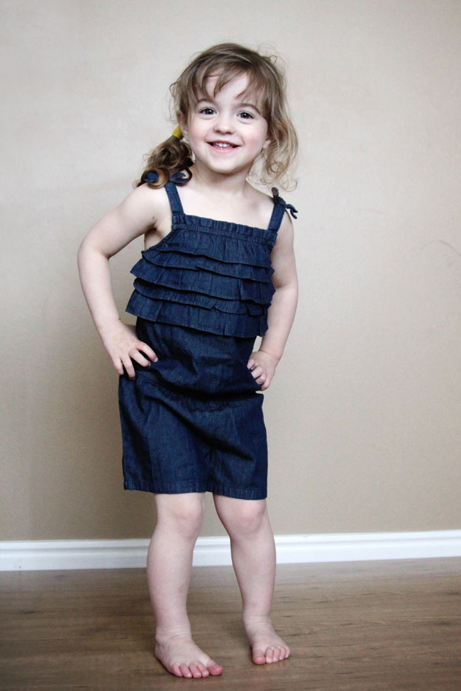 A little girl posing for a picture in front of a brown wall standing on a wood floor