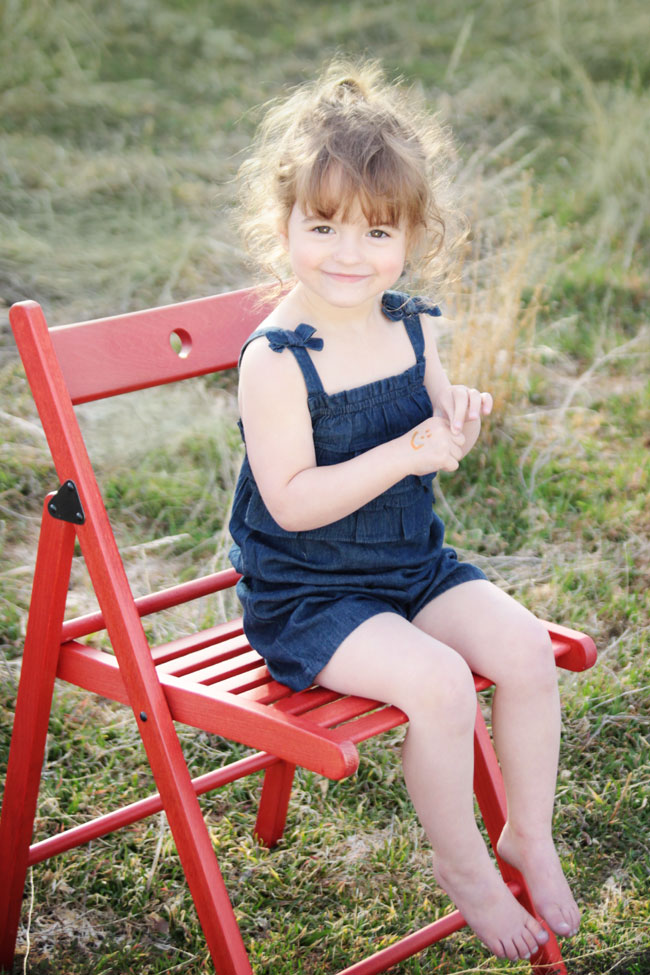 A little girl sitting on a red wood chair on the grass