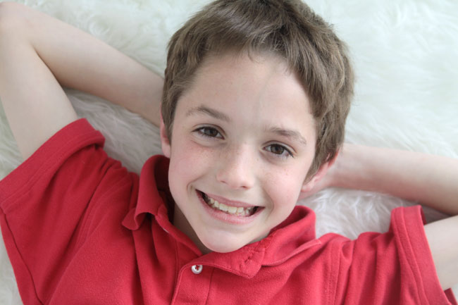 A young boy laying on a white faux fur rug with his hands behind his head
