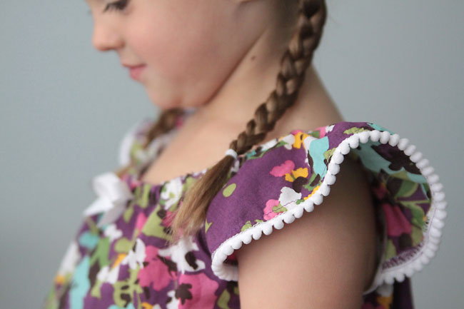 A close up of a girl wearing a purple shirt with pom pom trim on the sleeve