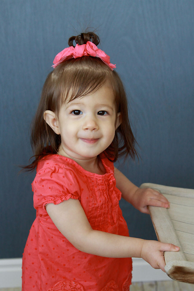 A little girl standing up holding onto the edge of a chair