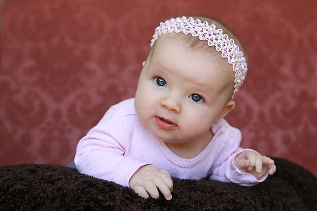 A baby on her front on a blanket lifting up her head to look at the camera